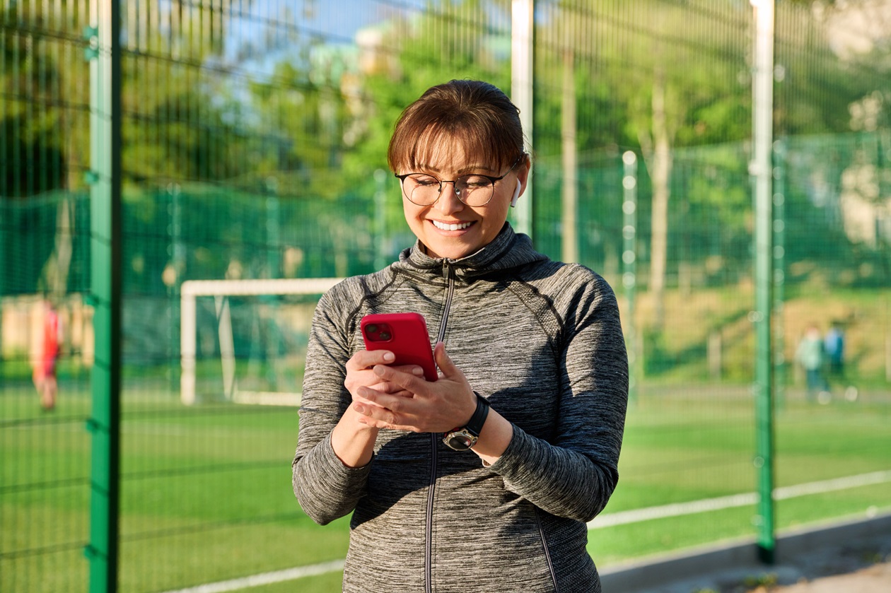 Active mature woman in sportswear headphones with smartphone, outdoor